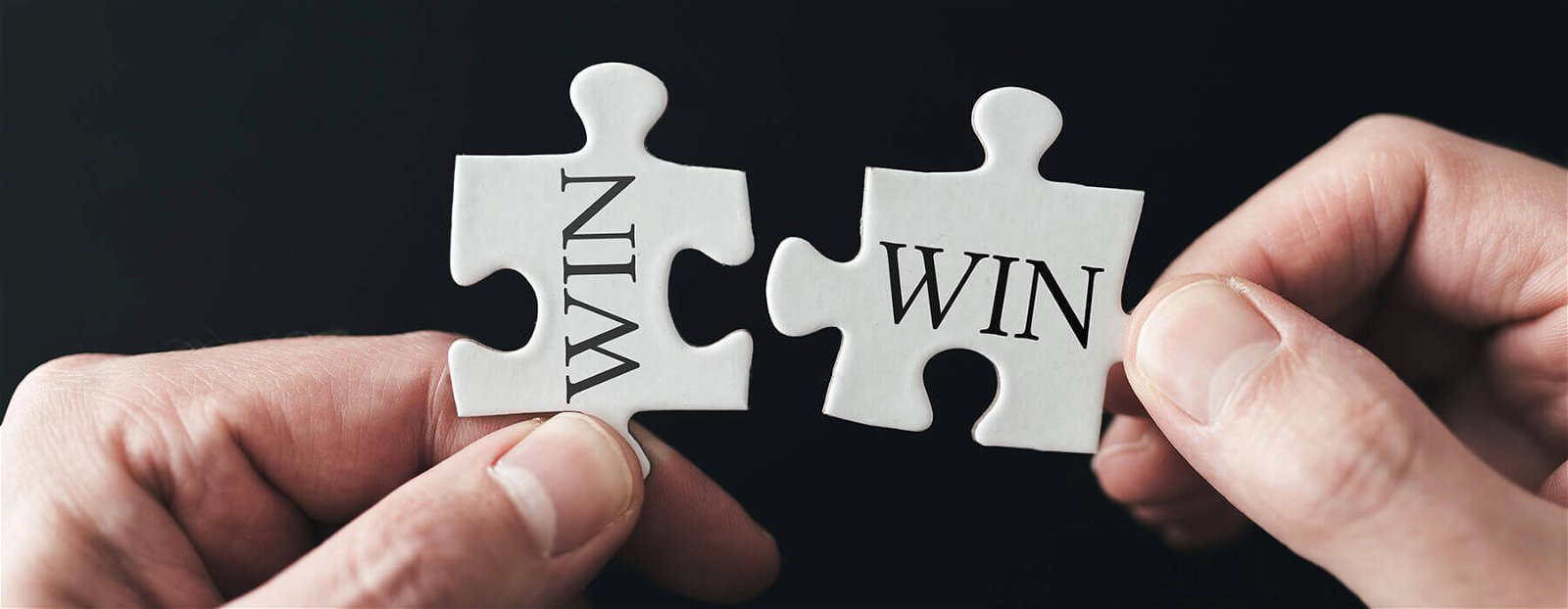 a set of hands try and fit two mismatched puzzle pieces that say "win" together